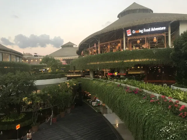 Open air mall terraces with thatched roofs, lit shopfronts and hedges of plants and flowers
