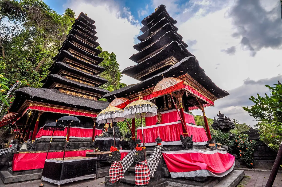 Two multi tiered meru towers above shrines draped in red cloth with ceremonial parasols