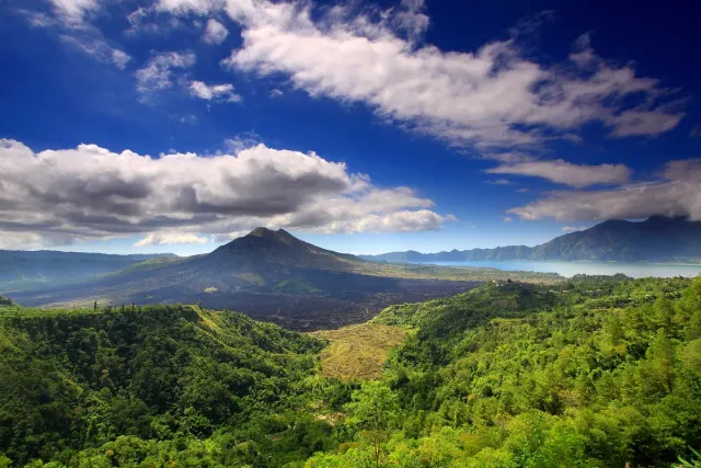 A view from above of a dark volcanic cone inside a green caldera, with a patch of blue lake at the right edge