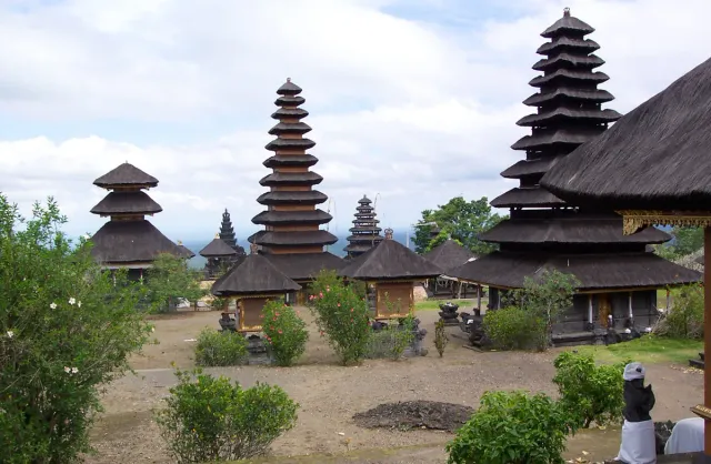 Meru towers with stacked thatched roofs in a wide temple courtyard, stone gates and greenery around