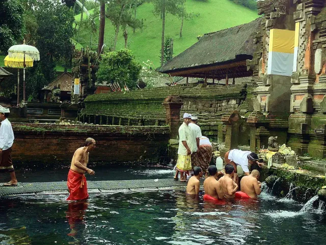 Worshippers standing in a water pool under a row of spring spouts, with temple pavilions and ceremonial umbrellas behind