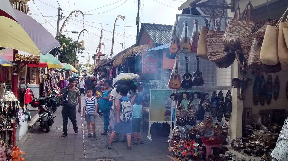 A shop lined street in Ubud with parasols and pedestrians