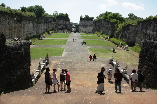 A wide avenue between tall cut limestone walls, with lawns and visitors walking along the path