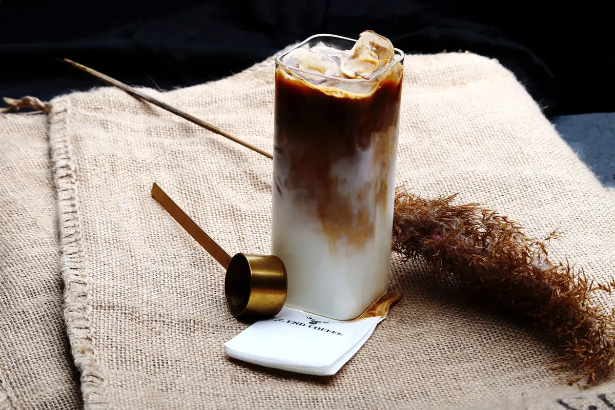 An iced coffee in a tall glass with a golden spoon