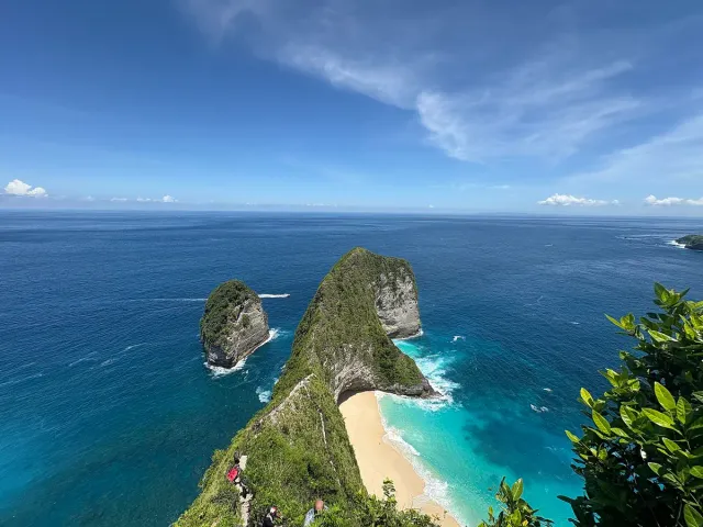 A green headland shaped like an animal head dropping to the sea, with a strip of white sand and turquoise water below