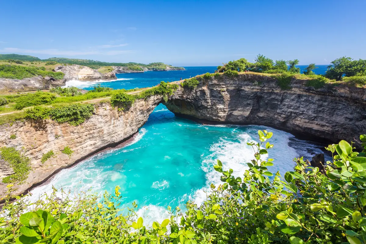 A round turquoise cove ringed by cliffs with a natural rock arch
