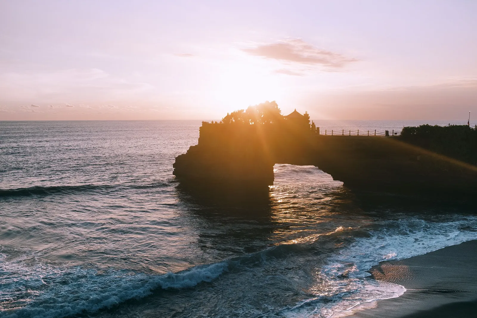 The sea temple of Tanah Lot silhouetted on its rock outcrop against an orange sunset sky in Bali