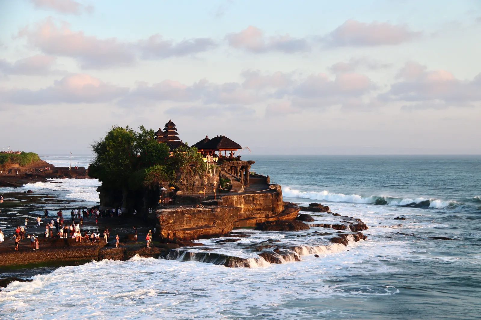 Visitors walking along the shoreline path towards Tanah Lot temple at low tide, Bali